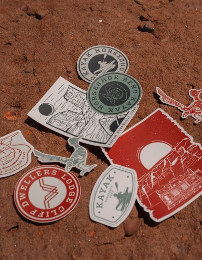 cliffdwellers general store (52) Assorted outdoor-themed stickers on red sandy ground